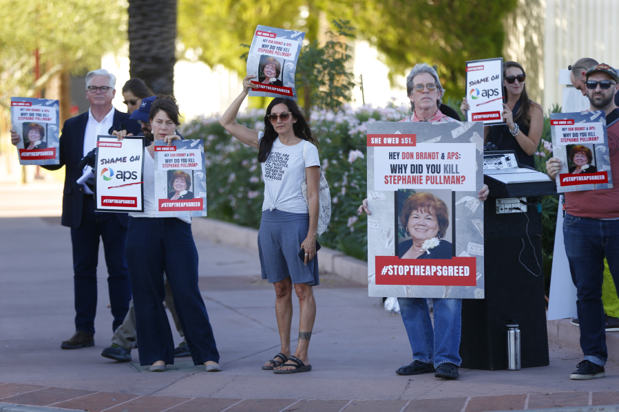 FILE - Stacey Champion, center, holds up a sign with Stephanie Pullman's picture during a protest outside of the Phoenix Art Museum where the Arizona Chamber of Commerce and Industry awards ceremony was celebrating Don Brandt, CEO of Arizona Public Service in Phoenix, Ariz., June 20, 2019. Pullman died in her home after her electricity had been shut off.