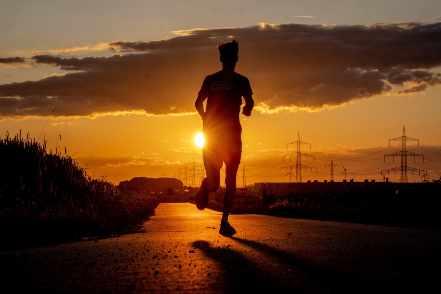 A man runs along a small road on the outskirts of Frankfurt, Germany, as the sun rises early Thursday, July 13, 2023.
