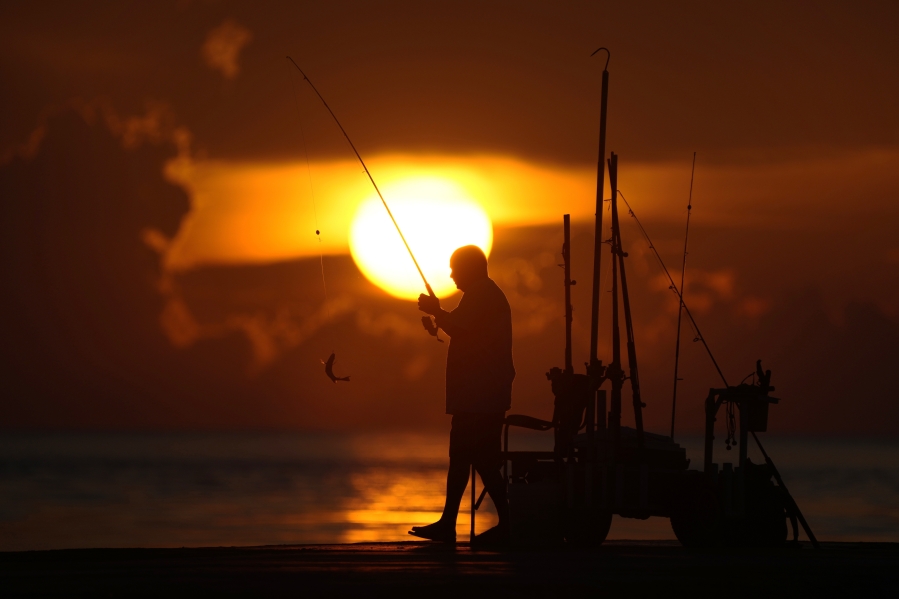 FILE - A fisherman reels in his catch as the sun rises over the Atlantic Ocean, June 28, 2023, in Bal Harbour, Fla. An already warming Earth steamed to its hottest June on record, with global oceans setting temperature records for the third straight month, the U.S. National Oceanic and Atmospheric Administration announced Thursday, July 13.