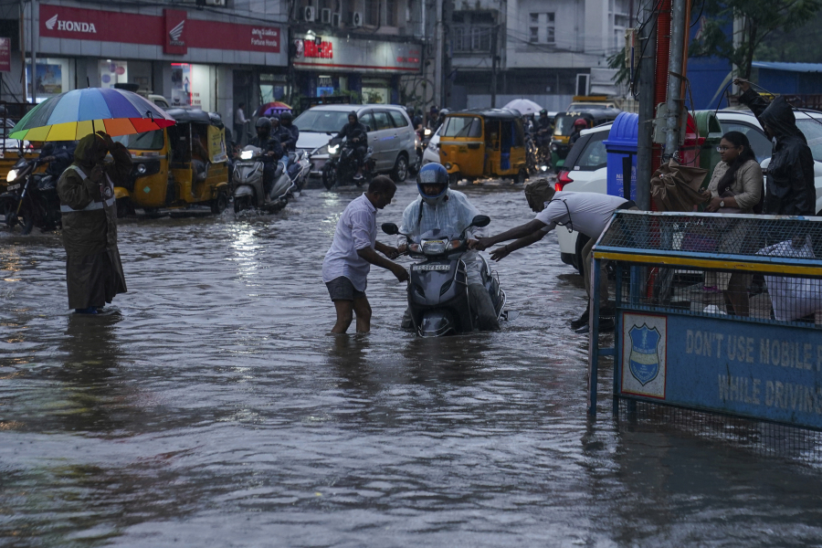 A traffic police officer, right and a man, left help a motorist at a water logged street during rain in Hyderabad, India, Thursday, July 20, 2023. India receives its monsoon rains from June to October.