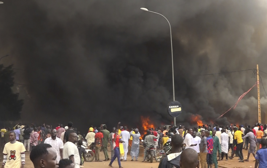 With the headquarters of the ruling party burning in the back, supporters of mutinous soldiers demonstrate in Niamey, Niger, Thursday, July 27 2023. Governing bodies in Africa condemned what they characterized as a coup attempt Wednesday against Niger's President Mohamed Bazoum, after members of the presidential guard declared they had seized power in a coup over the West African country's deteriorating security situation.