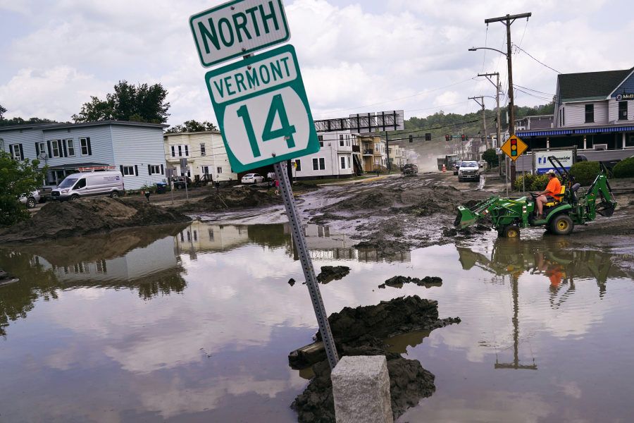 A small tractor clears water from a business as flood waters block a street, Wednesday, July 12, 2023, in Barre, Vt. Following a storm that dumped nearly two months of rain in two days, Vermonters are cleaning up from the deluge of water.