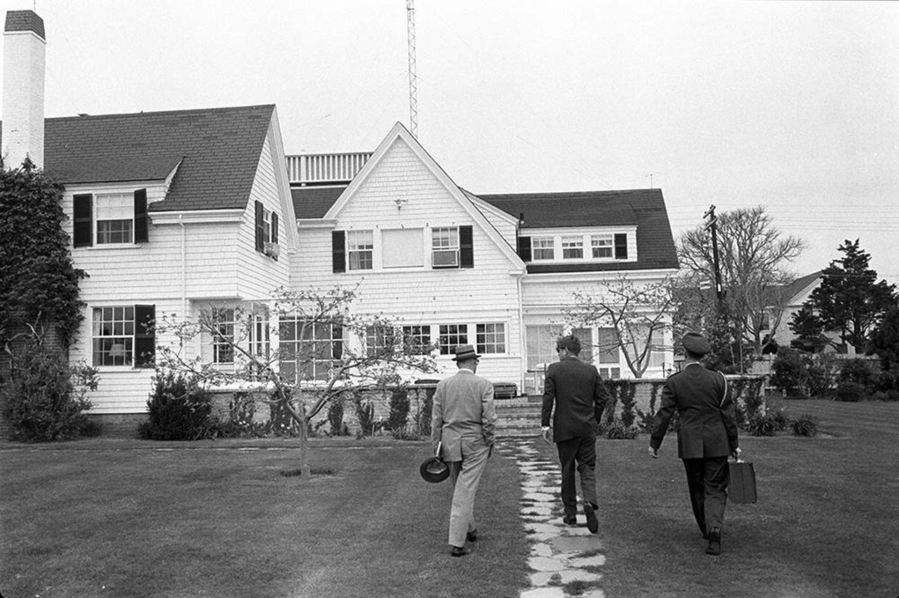 In this photo obtained by the National Security Archive from the John F. Kennedy Presidential Library, White House military aide Gen. Chester Clifton carries the Presidential Emergency Satchel with Kennedy and David Powers, approaching the "cottage" at Hyannis Port, Mass., on May 10, 1963, where Kennedy met with Canadian Prime Minister Lester Pearson. (John F.