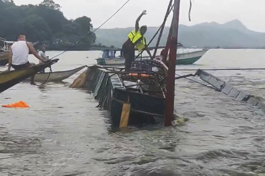 In this image from video provided by the Philippine Coast Guard, a man stands on a capsized passenger boat as they undergo rescue operations at Binangonan, Rizal province, east of Manila, Philippines on Thursday July 27, 2023. The Philippine passenger boat carrying dozens of people, including children, overturned Thursday after being lashed by strong wind in a town southeast of Manila and search and rescue efforts were underway, the Coast Guard said.