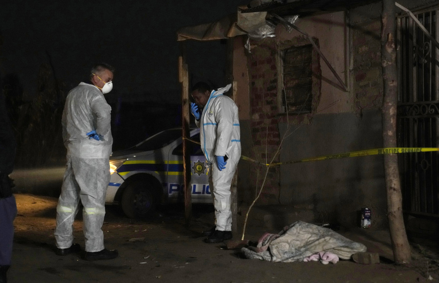 Police stand near a covered body in the Angelo settlement in Boksburg, South Africa, Thursday, July 6, 2023. Police said over a dozen people, including children, have died from a toxic gas leak in the informal settlement.