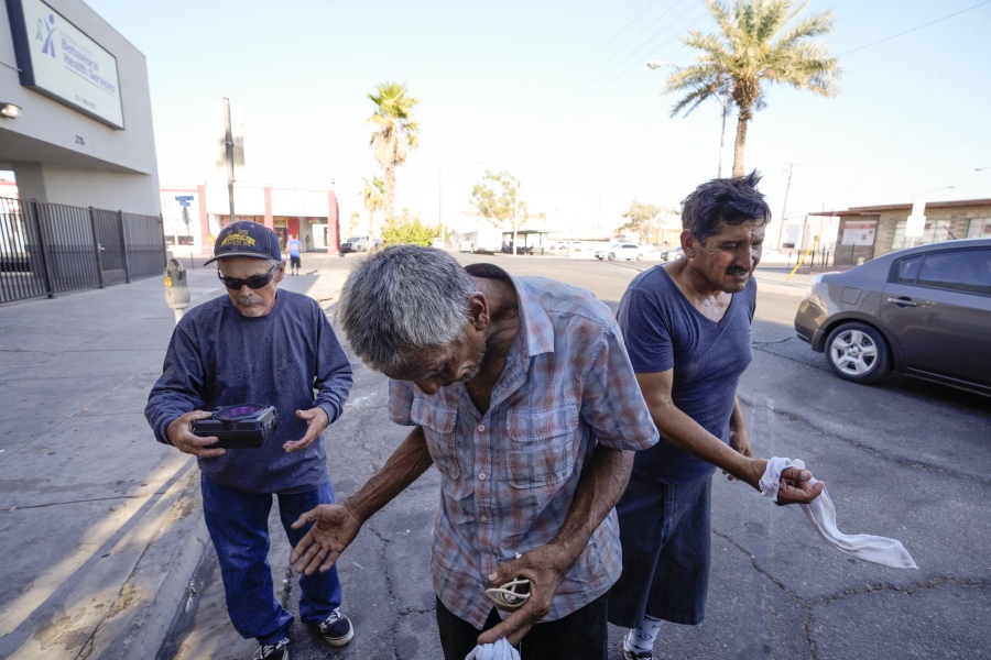 Three men, who are homeless, react as they are given cold, wet towels by Maribel Padilla of the Brown Bag Coalition, July 20, 2023, in Calexico, Calif. Once temperatures hit 113 degrees Fahrenheit (45 Celsius), Padilla and the Brown Bag Coalition meet up with people who are homeless in Calexico, providing them with cold, wet towels, and some refreshments to help them endure the scorching temperatures.