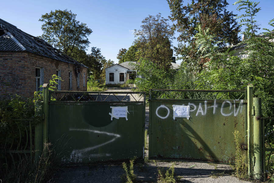 A gate stands in front of a former health clinic, background center, that had been used by Russian soldiers in Izium, Ukraine, Wednesday, Sept. 21, 2022. Ukrainian civilians said they were detained and tortured at the site.