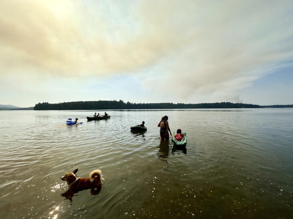 Smoke from a brush fire in Mason County rises to the sky as people float in Totten Inlet near Olympia, Wash., on Tuesday, July 4, 2023. A brush fire that started Tuesday is threatening homes and prompting evacuations near the western Washington city of Shelton. It was not immediately clear what caused the fire, which was estimated at more than 200 acres.