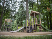 Trees rise above a playground at DuBois Park in Vancouver. The playground, which has a wheelchair user-friendly disc swing, is not considered fully accessible due to the wood chip surface. At top, a disc swing hangs at the under-construction Marshall Park.