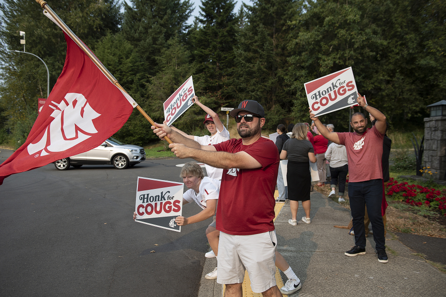 Jack Fisher, 15, from left, joins his brother, Will, 13, with maroon hat, their dad, P.J., black hat, who is a Washington State University alum, and Narek Daniyelyan, right, who is also an alum, as they greet students and staff on the first day of classes at Washington State University Vancouver on Monday morning (Amanda Cowan/The Columbian)