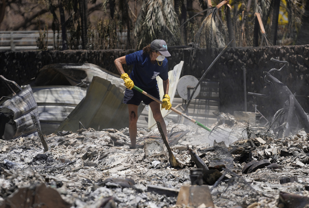A woman digs through rubble of a home destroyed by a wildfire, Friday, Aug. 11, 2023, in Lahaina, Hawaii.