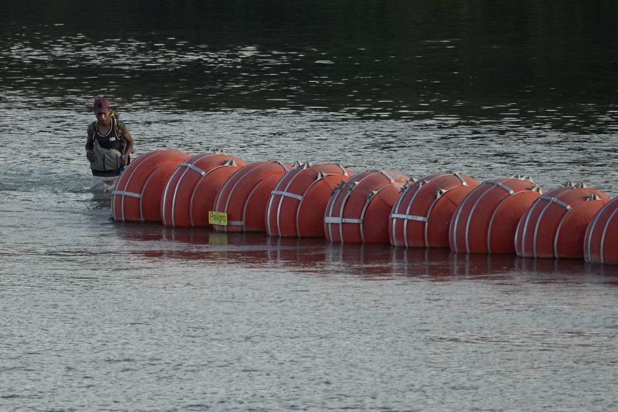 A migrant walks past large buoys being used as a floating border barrier Monday on the Rio Grande near Eagle Pass, Texas.