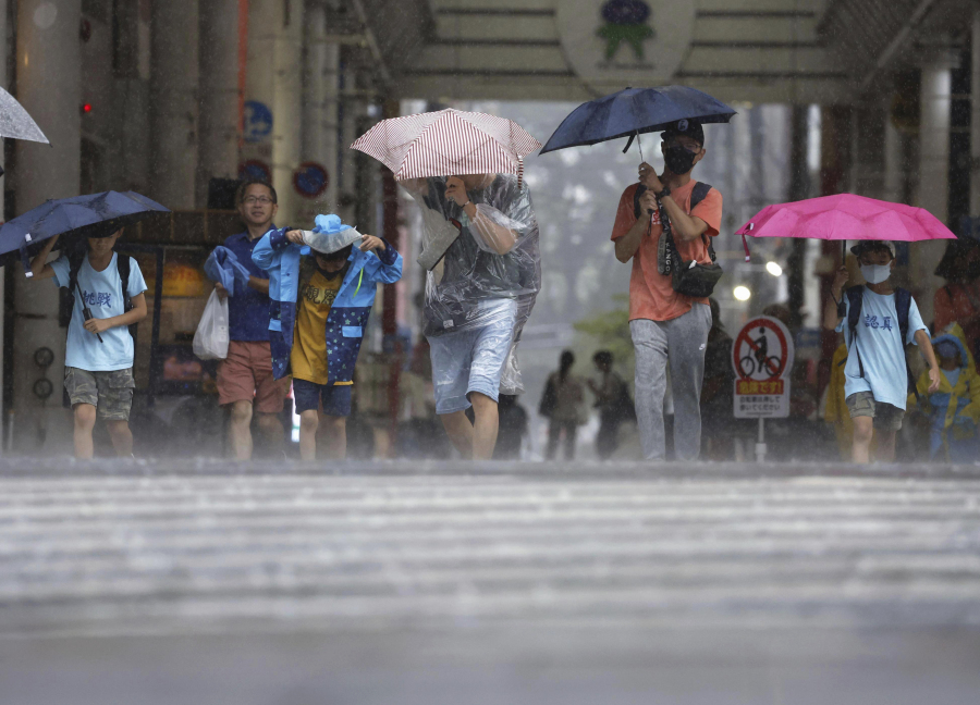 People walk across an intersection in a storm in Kagoshima, southern Japan, Tuesday, Aug. 8, 2023. Early Tuesday morning, the storm was centered 350 kilometers (217 miles) south of Kagoshima, a city on the southwestern tip of Japan's main southern island of Kyushu. Khanun produced winds of 108 kph (67 mph) with gusts to 144 kph (89 mph) and was slowly moving north, the Japan Meteorological Agency reported.