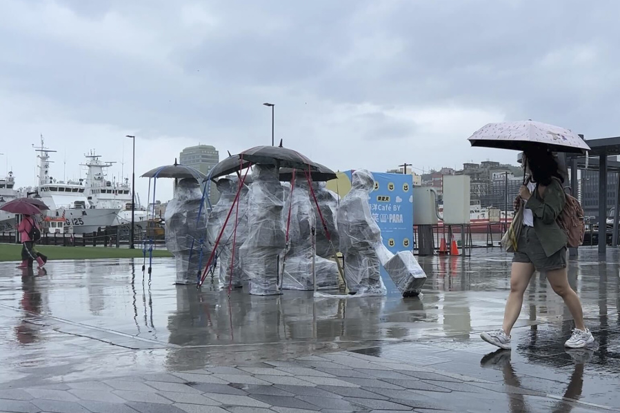 Residents with umbrellas walk past sculptures co covered up with plastic to protect from the incoming typhoon Khanun in the port city of Keelung near Taipei in northern Taiwan on Thursday, Aug. 3, 2023.