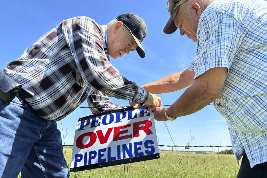 Gaylen Dewing, left, and Marvin Abraham affix a sign to a roadside fence east of Bismarck, N.D., on Tuesday, Aug. 15, 2023. The sign reads "People over pipelines," and is in opposition to Summit Carbon Solutions' proposed five-state, 2,000-mile pipeline network to carry carbon dioxide emissions from dozens of Midwestern ethanol plants to North Dakota for permanent storage deep underground.