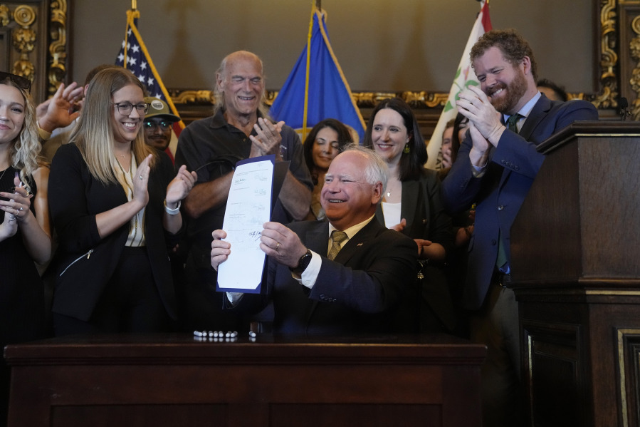 FILE - Minnesota Gov. Tim Walz, middle, holds the bill signed to legalize recreational marijuana for people over the age of 21, making Minnesota the 23rd state to do so, May 30, 2023, in St. Paul, Minn. Former Gov. Jesse Ventura stands at center. Fueled by election gains, Democrats in Minnesota and Michigan this year enacted far-reaching policy changes that party leaders aspire to replicate on the national stage and in other states.