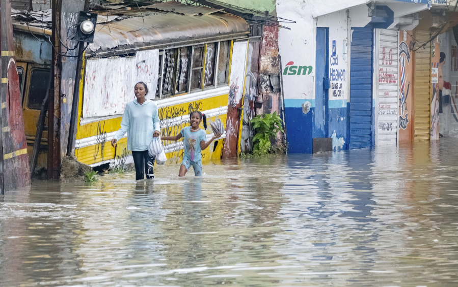 People walk through a street flooded by the rains of Tropical Storm Franklin in Santo Domingo, Dominican Republic, Tuesday, Aug. 22, 2023.