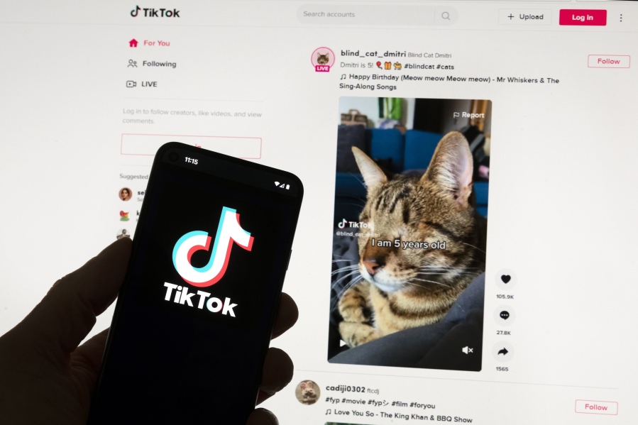 The TikTok logo is seen on a mobile phone in front of a computer screen which displays the TikTok home screen, Saturday, March 18, 2023, in Boston. Google, Facebook, TikTok and other Big Tech companies operating in Europe are facing one of the most far-reaching efforts to clean up what people encounter online.