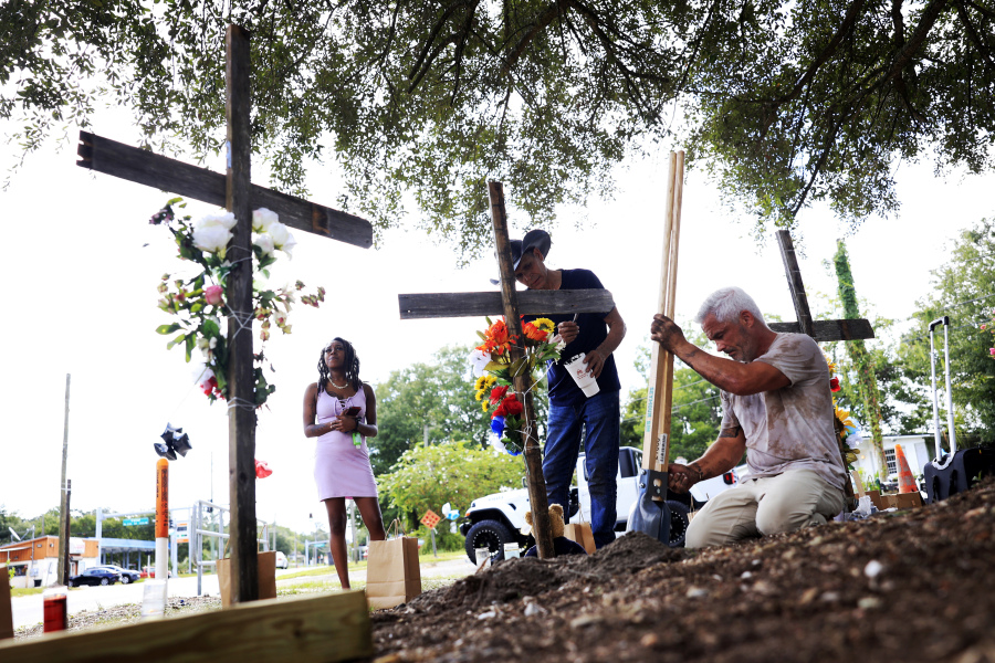 From left, a woman who goes by the name of "Queen," views crosses put up in memory of the victims of Saturday's shooting as artist Roberto Marquez, of Dallas, paints and Will Walsh, of Nocatee, Fla., helps construct posts Monday, Aug. 28, 2023, near the site of the attack at a Dollar General store in Jacksonville, Fla. Queen says she is a manager at the store and was holed up in the office at the store when the shooting occurred.