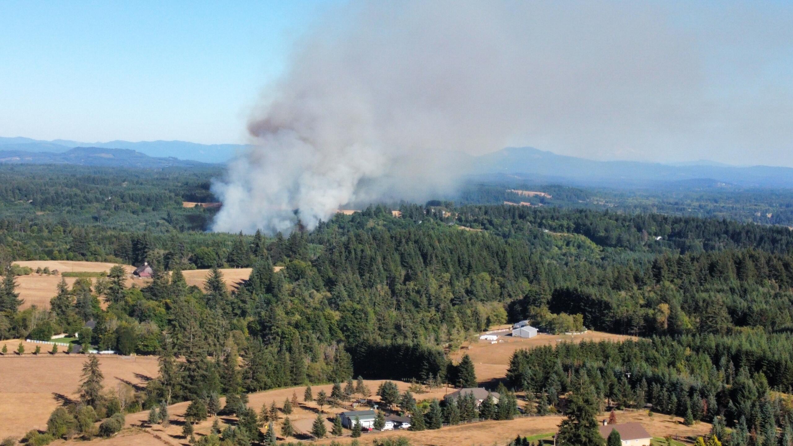 Smoke rises from a fire in a rural area near Northeast Jenny Creek Road on Wednesday afternoon. The fire began with a house fire that spread to nearby brush, prompting an evacuation of residences within a mile of the fire.