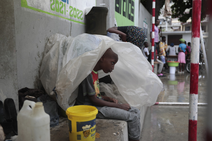 A youth displaced by the gang violence living at a school sits under plastic as rain from Tropical Storm Franklin falls in Port-au-Prince, Haiti, Wednesday, Aug. 23, 2023.