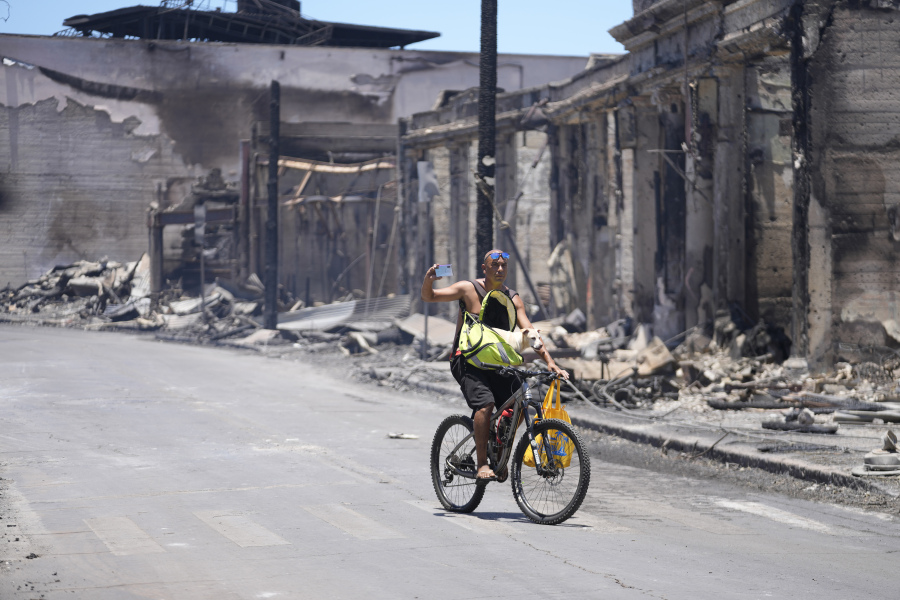A man and dog ride along Main Street past wildfire damage on Friday in Lahaina, Hawaii.