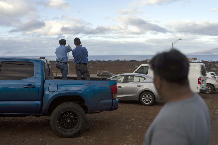 Wilfred Bulosan, left, and Fred Tomas stand on the bed of a pickup truck next to a checkpoint in Lahaina, Hawaii, Wednesday, Aug. 16, 2023, to view their homes consumed by a recent wildfire. (AP Photo/Jae C.