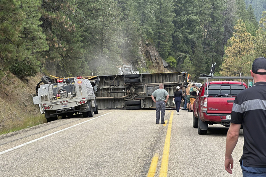 This image provided by Samantha Grange shows people looking on at the scene of an overturned school bus along Highway 55, Friday, Aug. 4, 2023, about 60 miles north of Boise, Idaho. The school bus carrying teenage campers rolled over on a winding Idaho highway Friday afternoon, injuring 11 people, the Idaho State Police said.