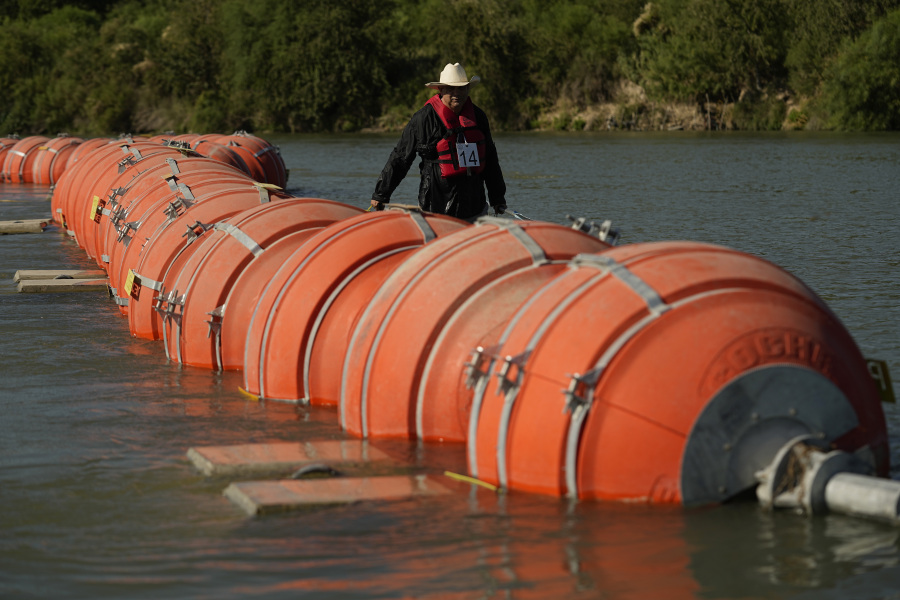 A kayaker walks past large buoys being used as a floating border barrier on the Rio Grande Tuesday, Aug. 1, 2023, in Eagle Pass, Texas.