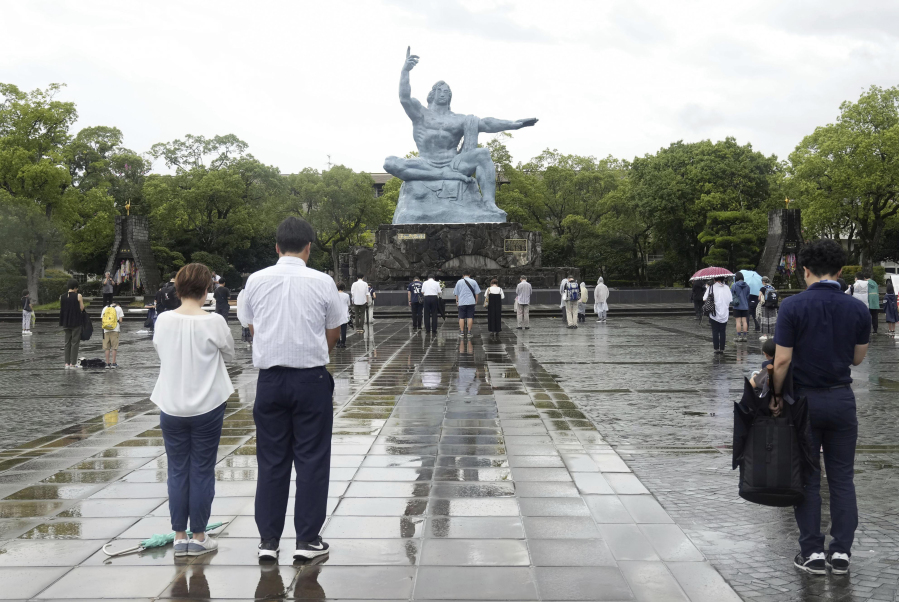 Visitors offer silent prayer for the victims of U.S. atomic bombing in front of the Peace Statue in Nagasaki, southern Japan Wednesday, Aug. 9, 2023, at the time when the bomb was dropped. The ceremony was held indoors and scaled down due to approaching Tropical Storm Khanun.