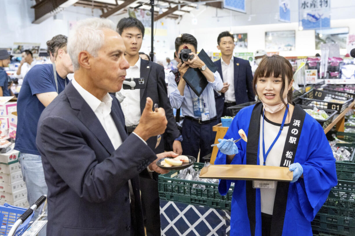 In this photo provided by U.S. Embassy, U.S. Ambassador to Japan Rahm Emanuel, left, eats peach samples at a market in Soma city, Fukushima prefecture, Thursday, Aug. 31, 2023. U.S. Ambassador Emanuel visited a northern Fukushima city Thursday and had seafood lunch with the mayor, talked to fishermen and stocked up on local produce at a grocery store to show they're all safe after the release of treated radioactive wastewater from the wrecked Fukushima Daiichi plant to the sea, backing Japan effort while criticizing China's ban on Japanese seafood as political.(U.S.