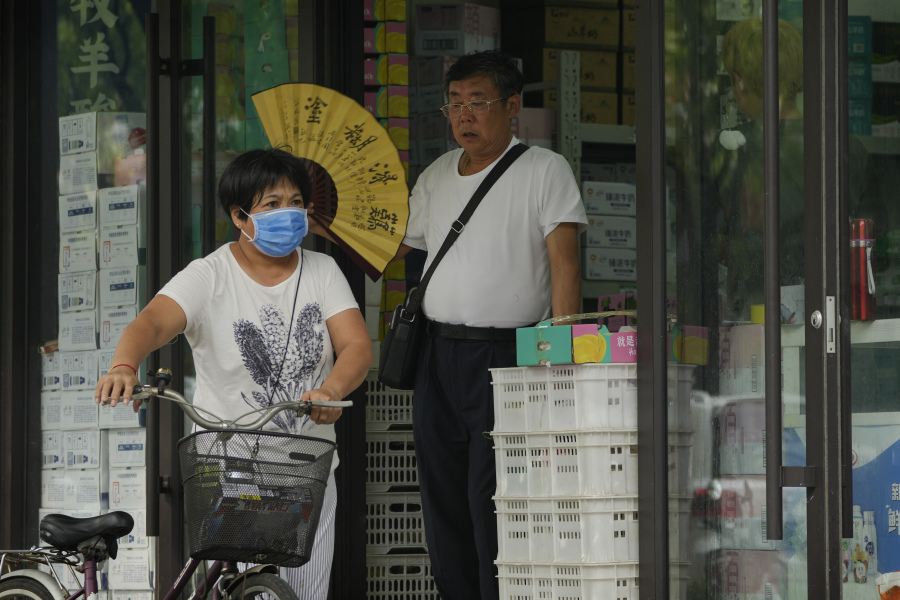 FILE - A woman pushes a bicycle past a man cooling himself with a fan at a store on a sweltering day in Beijing, July 24, 2023. Human-caused global warming made July hotter for four out of five people on Earth, according to a new report issued Wednesday, Aug. 2, 2023, by Climate Central.