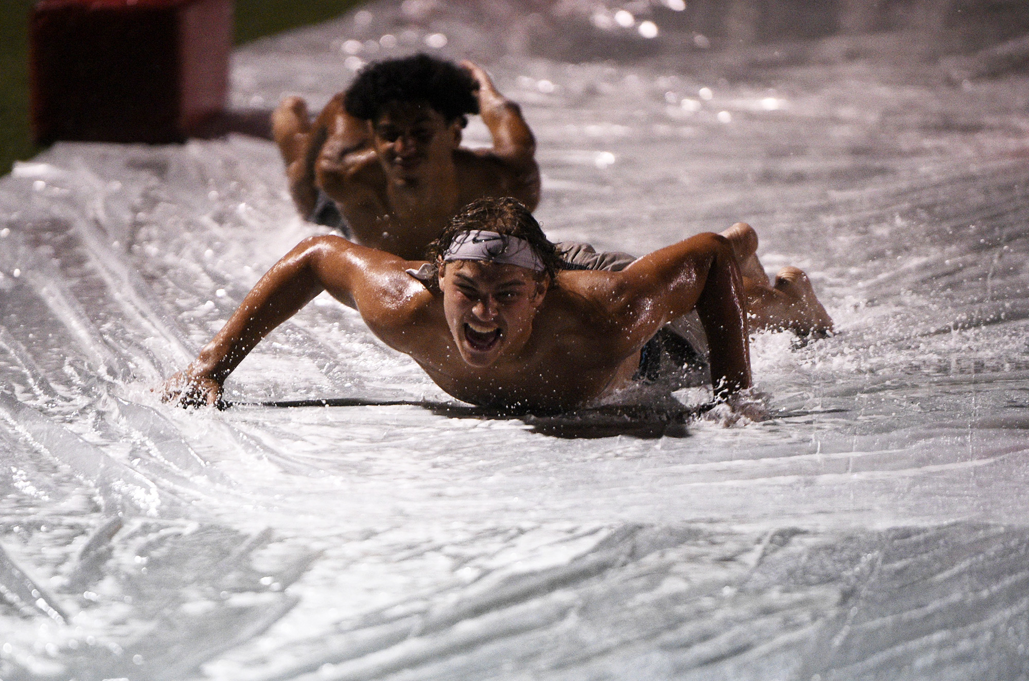 Prairie players slide down a Slip-N-Slide set on the field after the Falcons' midnight practice at Prairie High School on Wednesday, Aug. 16, 2023.