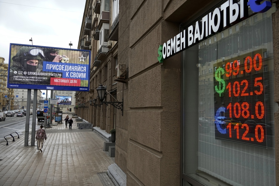 People walk past a currency exchange office with an army recruiting billboard calling for a contract for service in the Russian armed forces in Moscow, Russia, Monday, Aug. 14, 2023. The Russian ruble has reached its lowest value since the early weeks of the war in Ukraine as Western sanctions weigh on energy exports and weaken demand for the national currency.