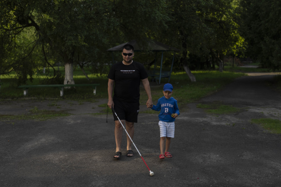 Denys Abdulin, a former Ukrainian soldier blinded in the war, walks with his son, Vadym, at a rehabilitation center designed for soldiers who lost their vision on the battlefield, near Rivne, Ukraine, Thursday, July 20, 2023. Over the course of several weeks, the veterans, accompanied by their families, reside at the rehabilitation center. Most receive their first canes here, take their first walks around urban and natural environments without assistance, and learn to operate programs on phones and computers. (AP Photo/Jae C.