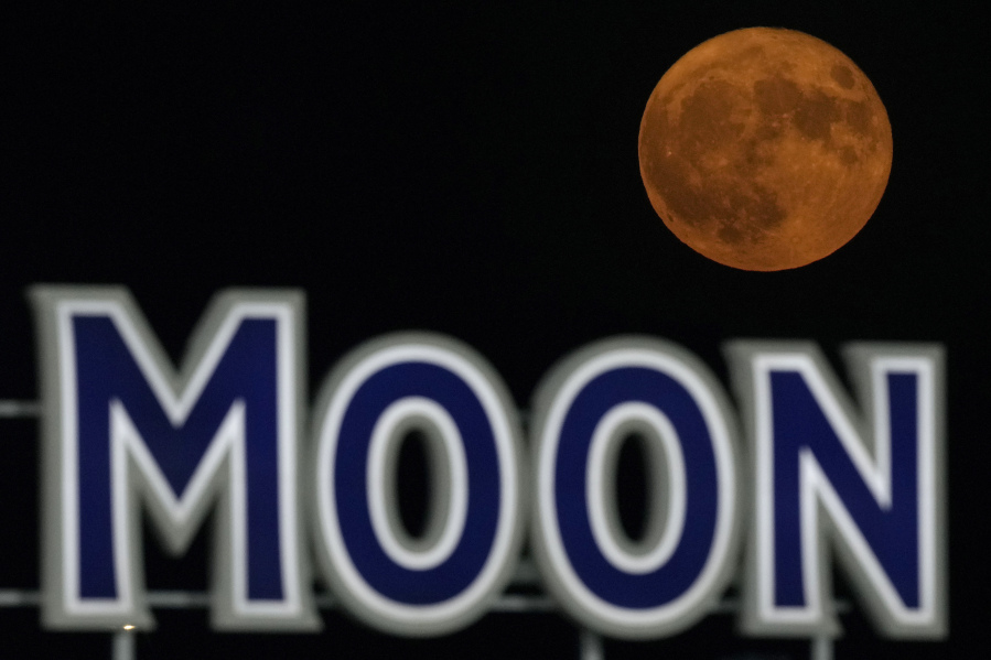 FILE - A supermoon rises beyond a beer sign at Kauffmann Stadium during a baseball game between the Kansas City Royals and the New York Mets, Aug. 1, 2023, in Kansas City, Mo. Stargazers are in for a double treat on Wednesday night, Aug. 30: a rare blue supermoon with Saturn peeking from behind. The cosmic curtain rises Wednesday night with the second full moon of August, the reason it's considered blue. It's dubbed a supermoon because it's closer to Earth than usual, appearing especially big and bright.
