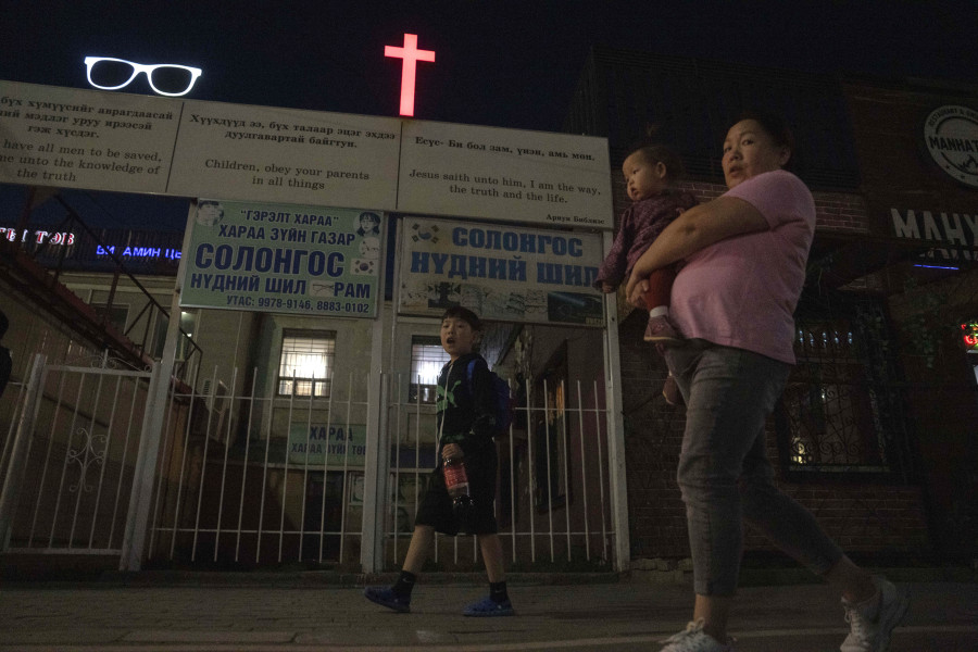 A woman carries a child past a cross and Christian quotes on the street in Ulaanbaatar, Mongolia on Tuesday, Aug. 29, 2023. When Pope Francis travels to Mongolia this week, he will in some ways be completing a mission begun by the 13th century Pope Innocent IV, who dispatched emissaries east to ascertain the intentions of the rapidly expanding Mongol Empire and beseech its leaders to halt the bloodshed and convert.