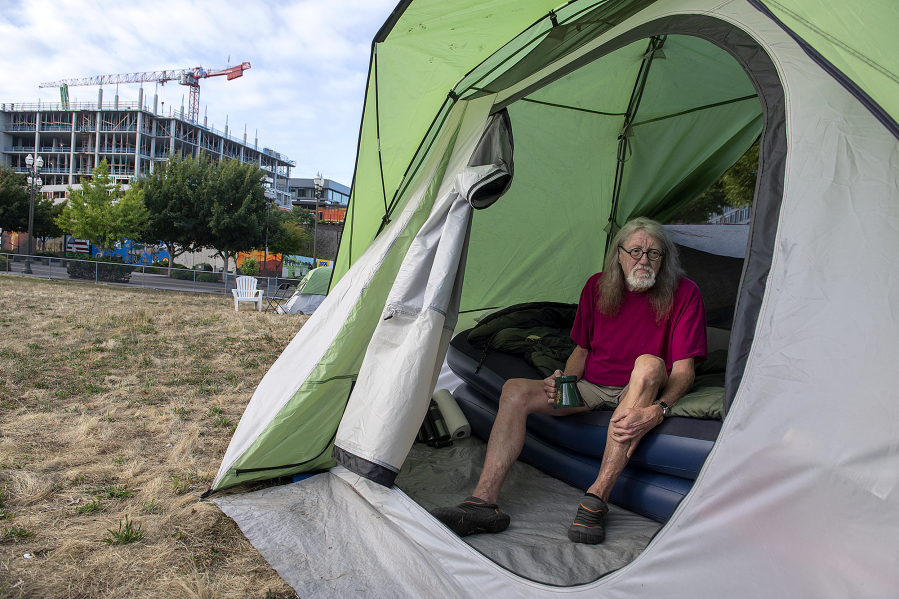 J.P. Walmer enjoys his morning coffee in his tent outside Vancouver City Hall as construction at the nearby waterfront is visible in the background. Walmer has been homeless for about a month and is looking for a place he can afford. He said he sleeps on multiple air mattresses to make it easier for him to get out of bed.