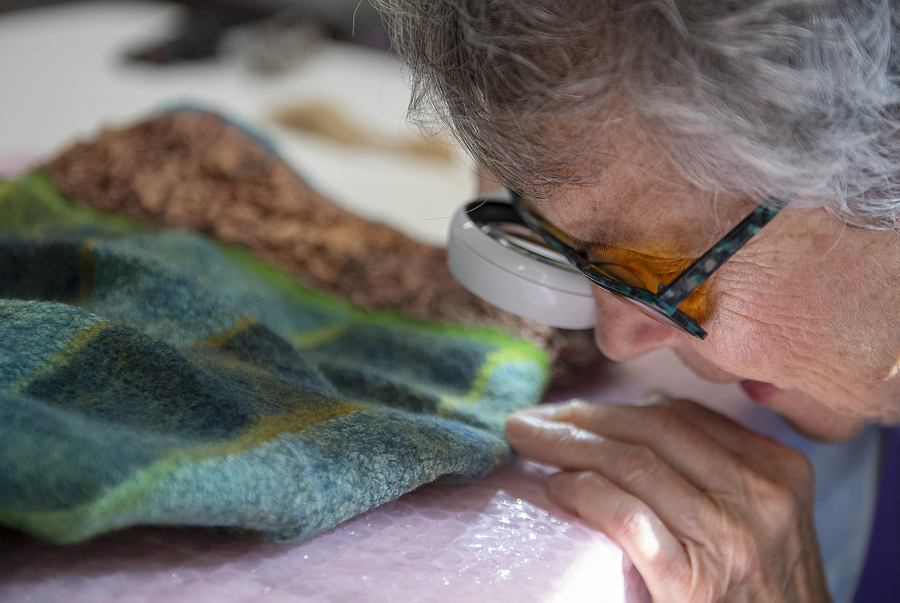 Visually impaired artist Patty White uses a strong handheld magnifier with a light to look over a felt hat she created in her Vancouver studio.