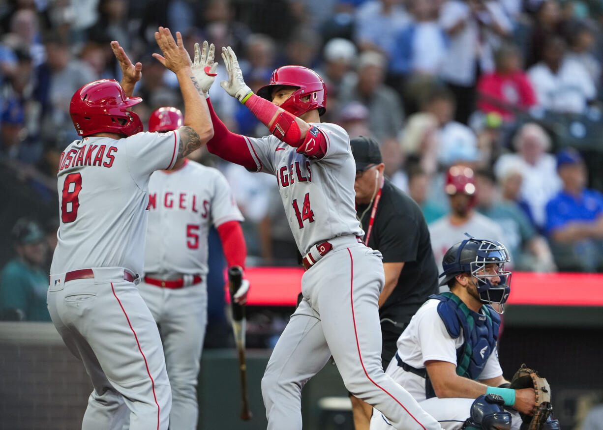 Los Angeles Angels' Logan O'Hoppe (14) is greeted by teammate Mike Moustakas (8) after scoring on his two-run home run off Seattle Mariners starting pitcher Logan Gilbert during the second inning of a baseball game as Mariners catcher Cal Raleigh, right, looks on Monday, Sept. 11, 2023, in Seattle.