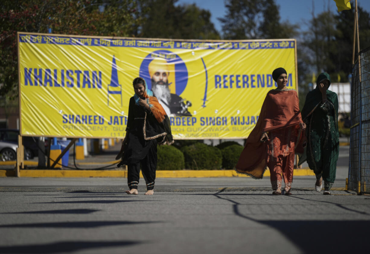Women walk past as a photograph of late temple president Hardeep Singh Nijjar on a banner outside the Guru Nanak Sikh Gurdwara Sahib in Surrey, British Columbia, on Monday, Sept. 18, 2023, where temple president Hardeep Singh Nijjar was gunned down in his vehicle while leaving the temple parking lot in June.