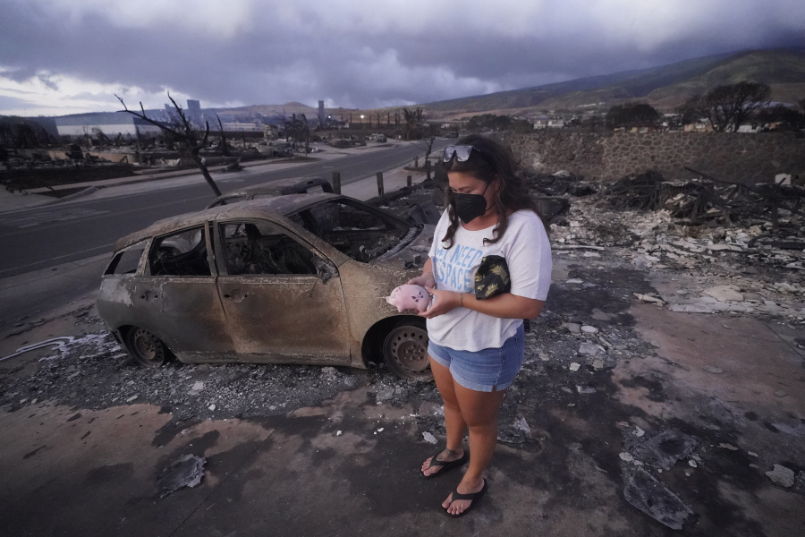 FILE - Summer Gerling picks up her piggy bank found in the rubble of her home following the wildfire on Aug. 10, 2023, in Lahaina, Hawaii.