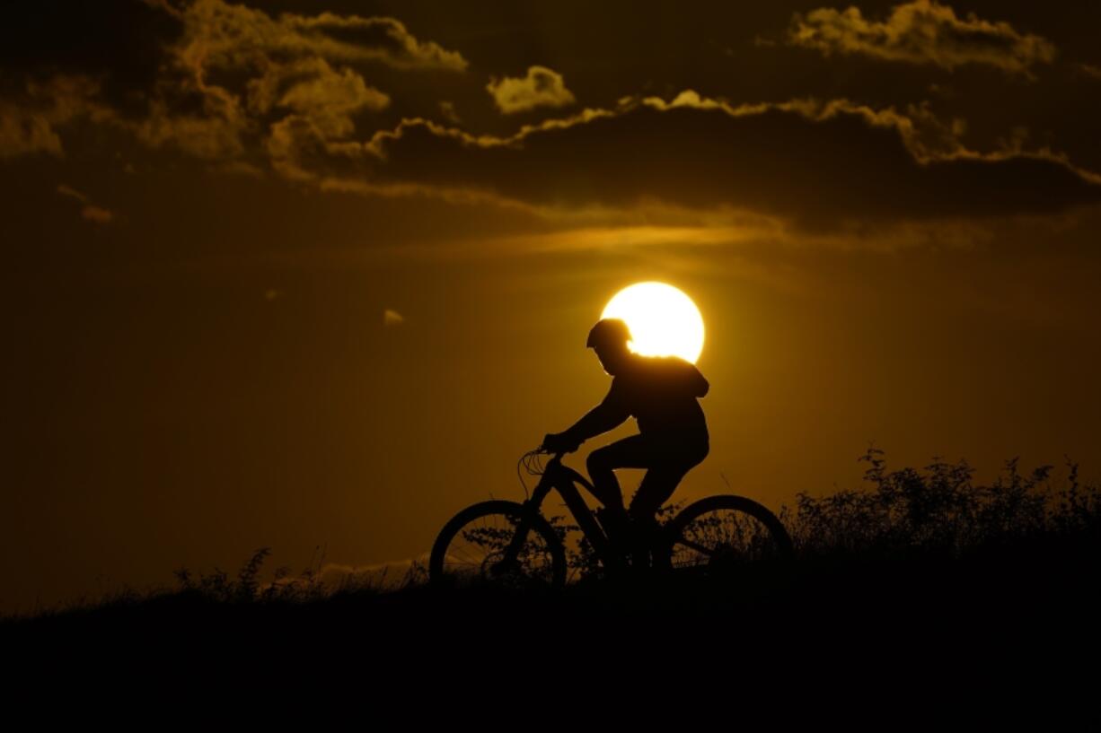 FILE - A cyclist tops a hill on a hot day at sunset, Aug. 20, 2023, in San Antonio. UN weather agency says Earth sweltered through the hottest summer ever as record heat in August capped a brutal, deadly three months in northern hemisphere.