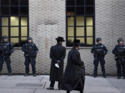Orthodox Jewish men pass New York City police guarding a Brooklyn synagogue on Dec. 11, 2019, prior to a funeral for Mosche Deutsch, a rabbinical student from Brooklyn who was killed in a shooting at a Jersey City, N.J., market. Ahead of the High Holidays, encompassing Rosh Hashana and Yom Kippur, that began this week, a network of Jewish security experts and religious leaders hosted several webinars to help prepare for the season.
