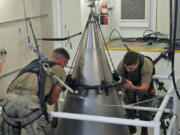 In this image provided by the U.S. Air Force, Senior Airman Jacob Deas, 23, left, and Airman 1st Class Jonathan Marrs, 21, right, secure the titanium shroud at the top of a Minuteman III intercontinental ballistic missile on Aug. 24, 2023, at the Bravo 9 silo at Malmstrom Air Force Base in Montana. After the shroud is secured, it is lifted off, revealing the black cone-shaped nuclear warhead inside. (John Turner/U.S.