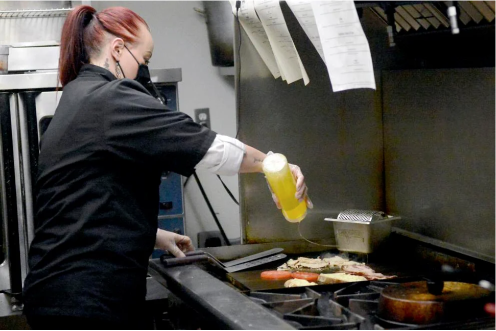 Creekside Cafe owner Danielle Rowley grills a turkey bacon melt in May 2021 at the Commerce Avenue restaurant. The business closed that November and still owes thousands of dollars in COVID fines, according to the state.