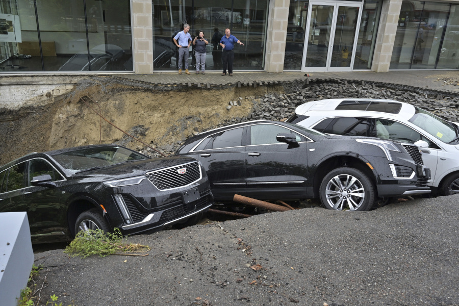 Rick Durand Owner of Durand Cadillac, left, and colleagues stand behind three vehicles that fell into a sinkhole that was washed out of his car dealership Tuesday, Sept. 12, 2023, in Leominster, Mass. after more than 9 inches of rain fell overnight.