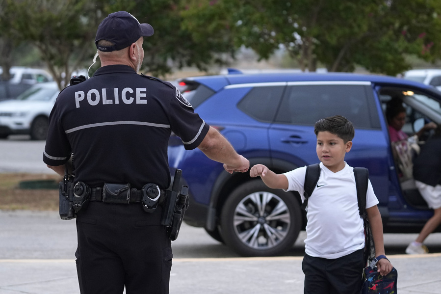 Southside Independent School District police officer Ruben Cardenas, left, greets a student arriving at Freedom Elementary School, Wednesday, Aug. 23, 2023, in San Antonio. Most Texas school districts say they are unable to comply with a new law requiring armed officers on every campus. The mandate was one of Republican lawmakers' biggest acts following the Uvalde school shooting in 2022 that killed 19 children and two teachers.
