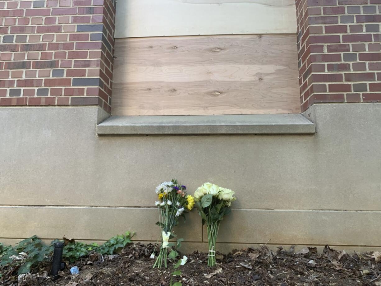 Flowers lay under a boarded up window at Caudill Labs on the UNC-Chapel Hill campus in Chapel Hill, N.C., Tuesday, Aug. 29, 2023, after a graduate student fatally shot his faculty adviser. A bullet hole could be seen earlier Tuesday in the bottom left corner of that window.