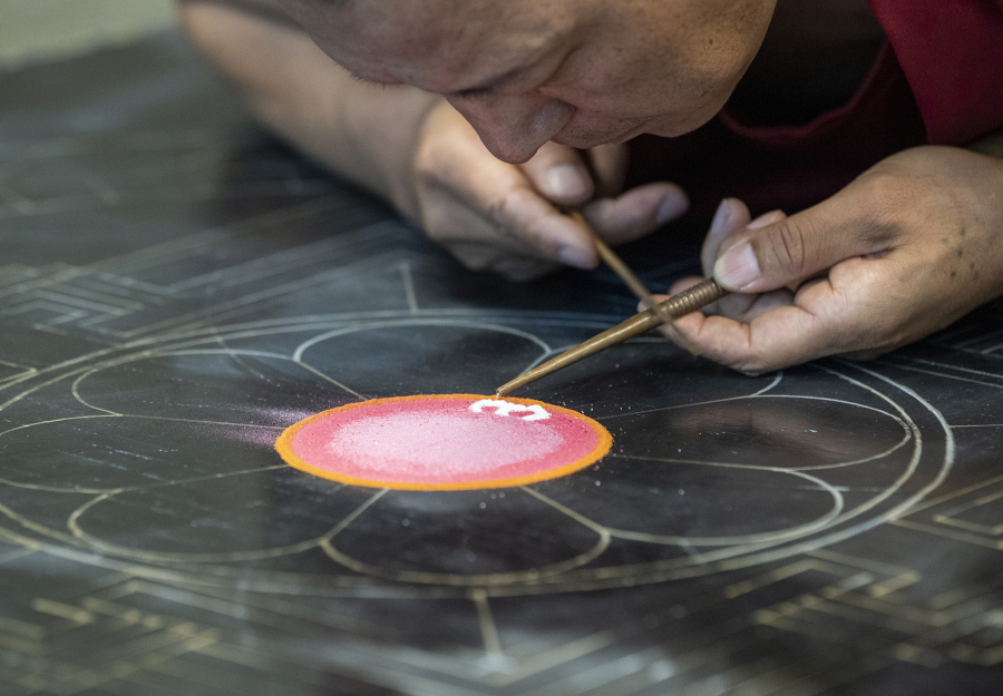 Tibetan Buddhist monk Nawang Shakga works on a sand mandala Monday at Clark College's Cannell Library. The mandala's creation began with the outline of a small orange circle at the very center, which was then filled with a soft pink.